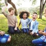 kids sitting in a circle playing in the park with their male nanny