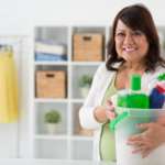 An executive housekeeper carrying cleaning supplies and smiling