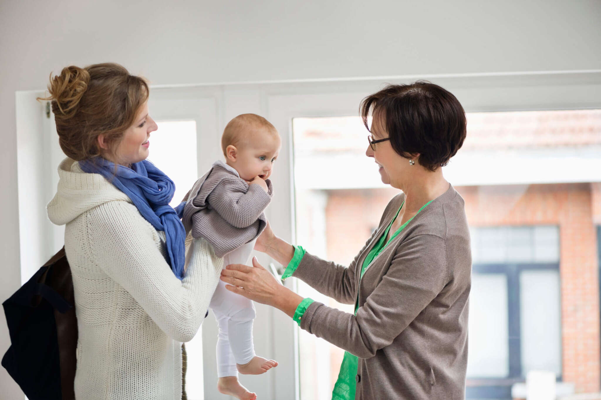 mother handing off young baby to newborn care specialist