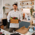 Private chef holding a crate of fresh vegetables in a modern kitchen, symbolizing personalized meal prep for special dietary needs.
