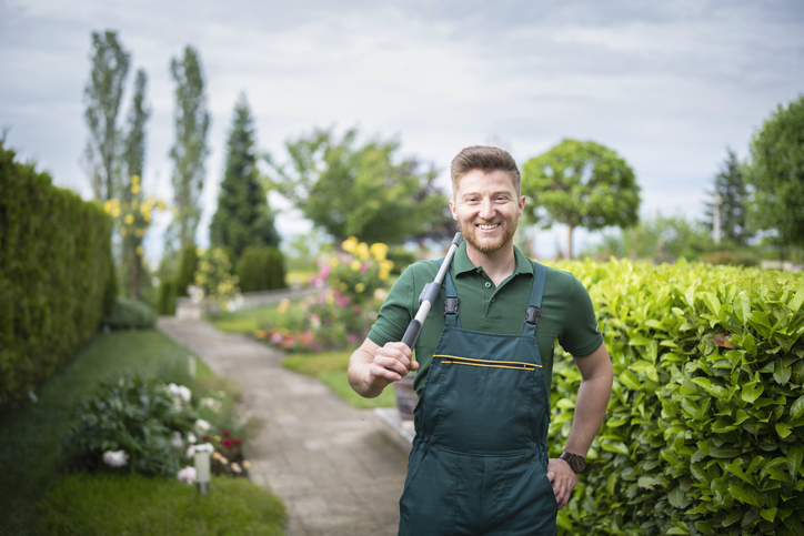 Smiling property manager/estate caretaker standing in a well-maintained garden with hedge clippers, symbolizing seasonal property management and year-round home maintenance.