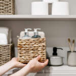 Housekeeper organizing linen closet shelves with labeled baskets and neatly stored bathroom essentials