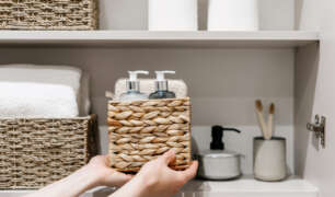 Housekeeper organizing linen closet shelves with labeled baskets and neatly stored bathroom essentials