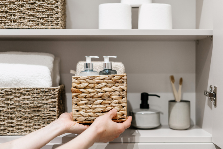 Housekeeper organizing linen closet shelves with labeled baskets and neatly stored bathroom essentials